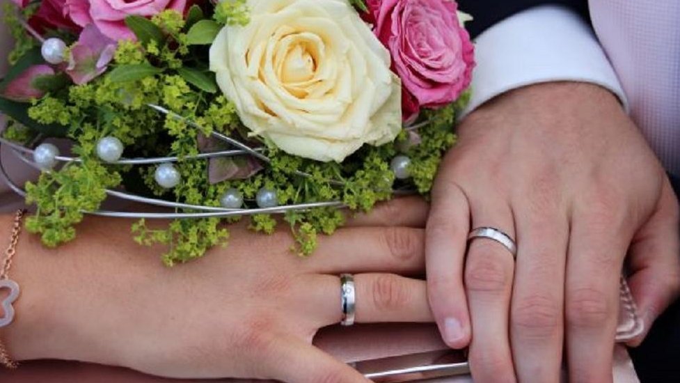 Hände mit Eheringen und ein Brautstrauß mit Rosen und Perlen